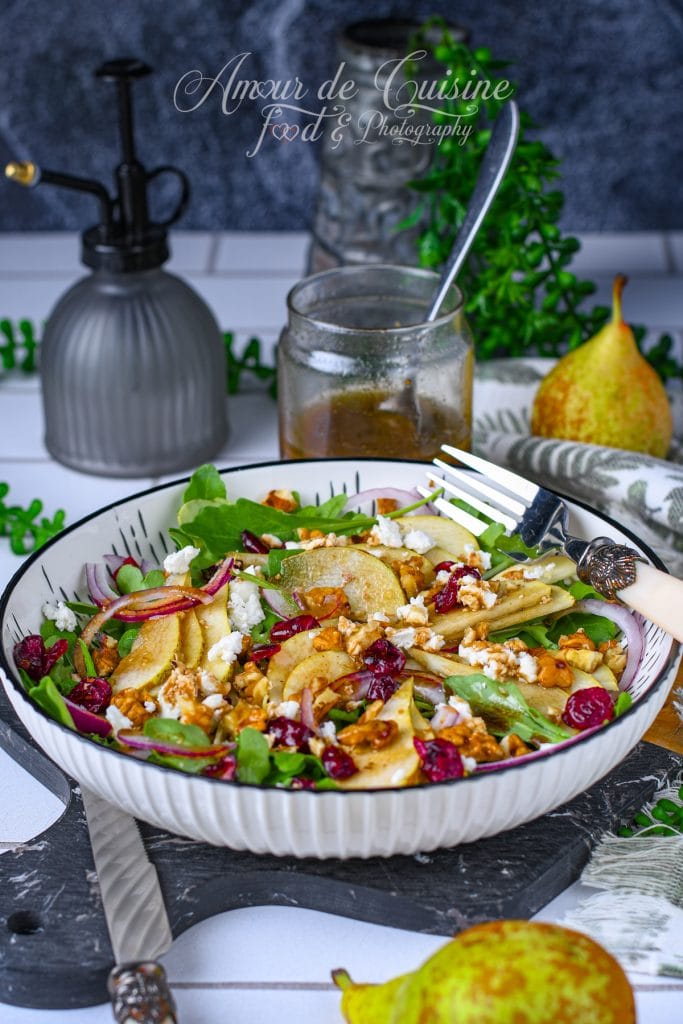 Salade aux poires, roquette, feta, noix et cranberries séchées, servie dans un grand bol avec vinaigrette balsamique-érable maison, garnie d’oignon rouge et présentée sur une table rustique.