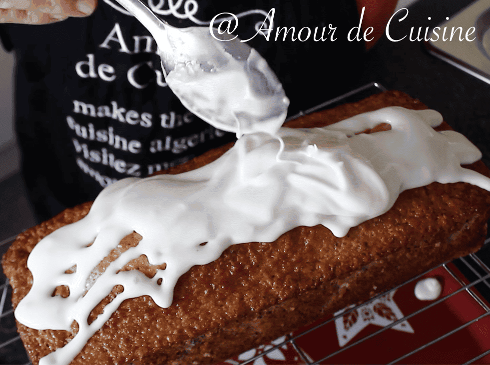 Homemade lemon loaf being topped with fresh lemon glaze using a spoon, cooling on a wire rack.