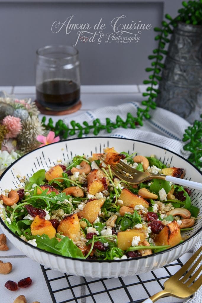 Salade de coings rôtis au quinoa et roquette, garnie de feta, noix de cajou et cranberries séchées, servie dans un bol sur une table décorée, avec une vinaigrette balsamique en arrière-plan.