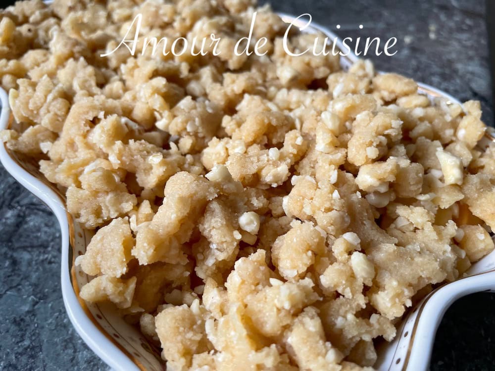 Pâte à crumble à la noisette émiettée sur des morceaux de coings dans un plat à gratin avant cuisson, montrant une texture sablonneuse et dorée prête à devenir croustillante au four.