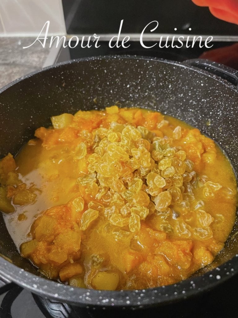 Cuisson de la mrouzia constantinoise dans une cocotte, avec des morceaux de potiron fondants et des raisins secs jaunes ajoutés en cours de préparation pour une texture sucrée et parfumée.