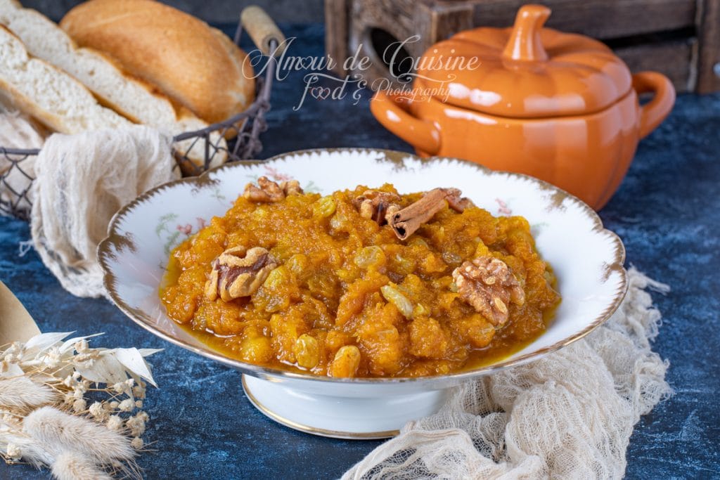 Assiette de mrouzia constantinoise, purée de potiron sucrée aux raisins secs et noix, décorée de bâtons de cannelle, servie sur une table rustique avec pain maison et soupière en céramique orange.