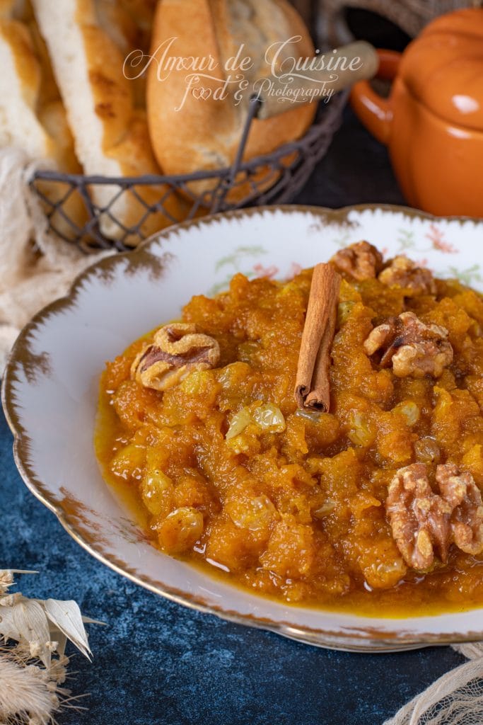 Assiette de mrouzia constantinoise, purée de potiron sucrée aux raisins secs et noix, décorée d’un bâton de cannelle, servie sur une table rustique avec du pain maison en arrière-plan