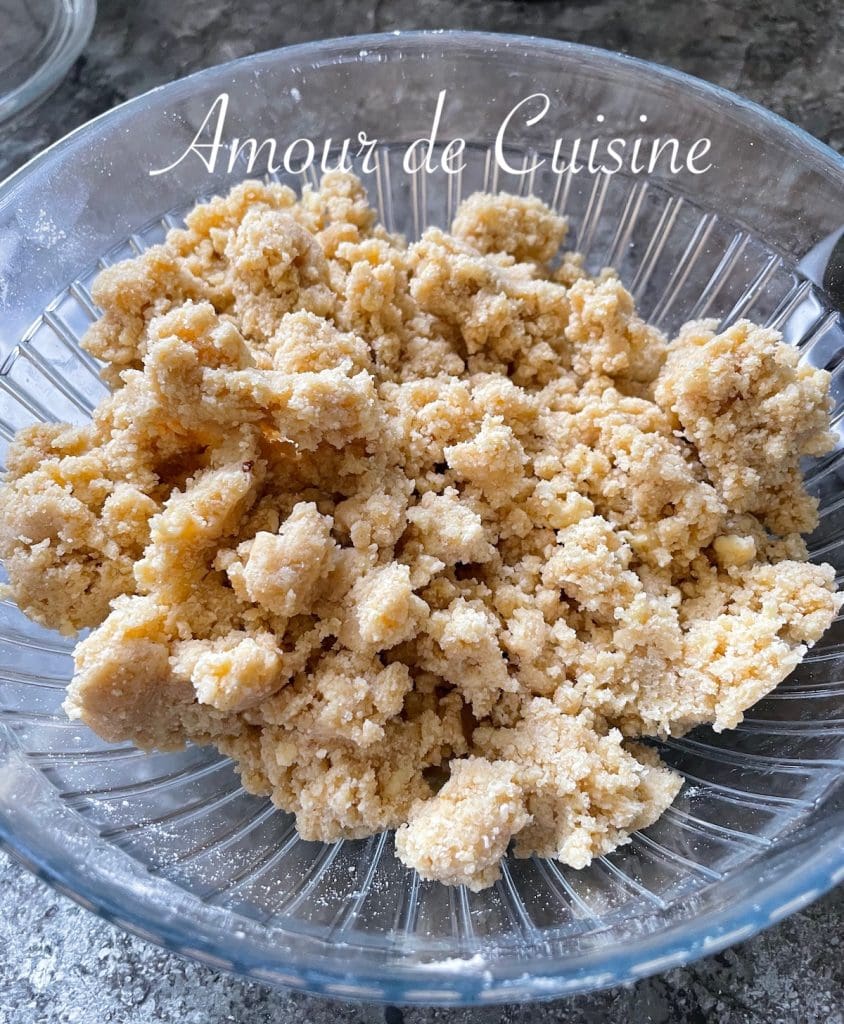 Saladier en verre rempli de pâte à crumble maison, à la texture sableuse et grumeleuse, prête à être utilisée pour un dessert gourmand.