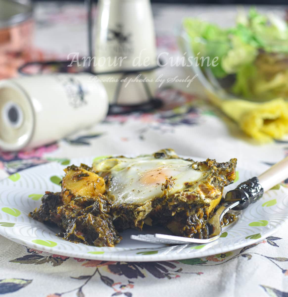 A plate of spinach and potato shakshuka with a soft-cooked egg on top, served with a fork on a floral tablecloth, surrounded by a rustic table setup and a fresh green salad in the background.