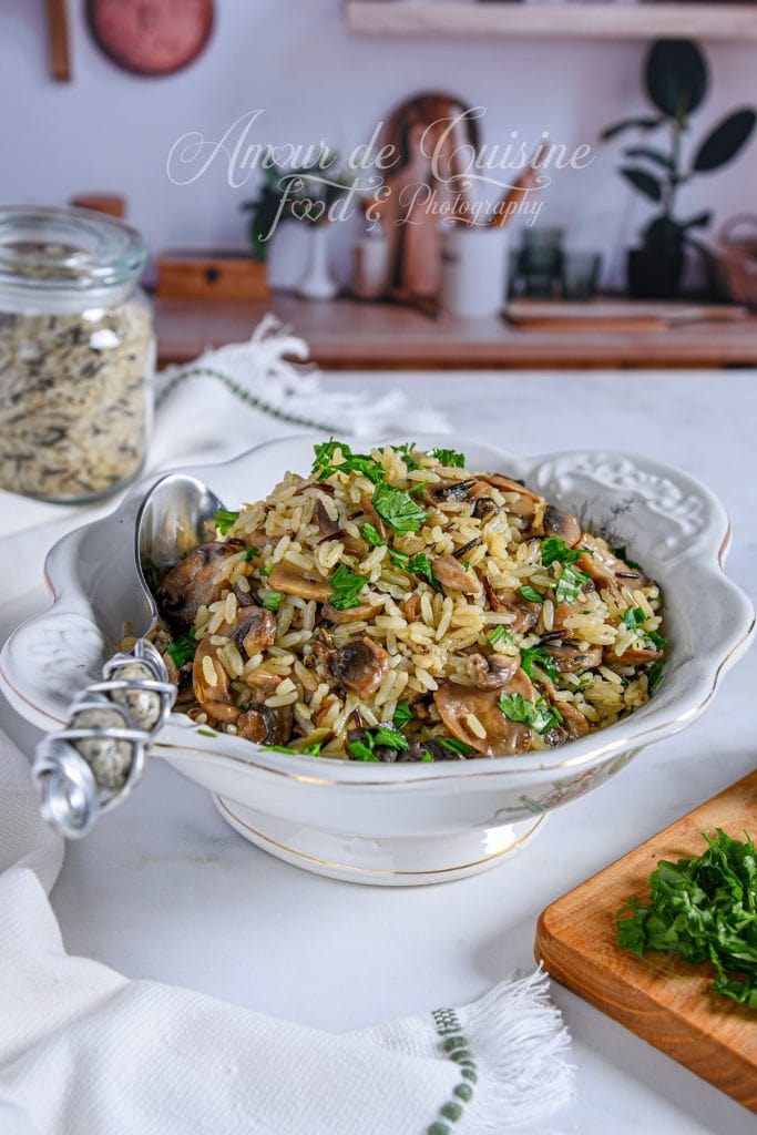 Bol de riz pilaf sauvage aux champignons, garni de persil frais, servi dans un plat blanc élégant sur un plan de travail de cuisine, avec un pot de riz sauvage en arrière-plan.