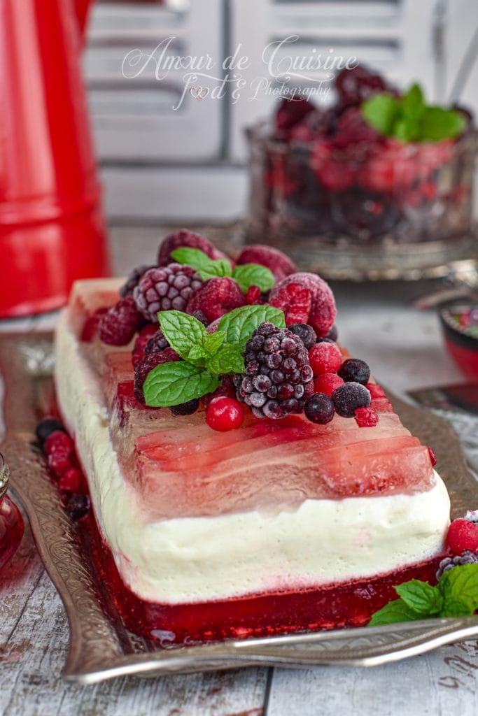 Layered panna cotta terrine with vanilla and red fruit jelly, topped with frozen berries and fresh mint, presented on a silver tray with vintage red and white kitchen decor