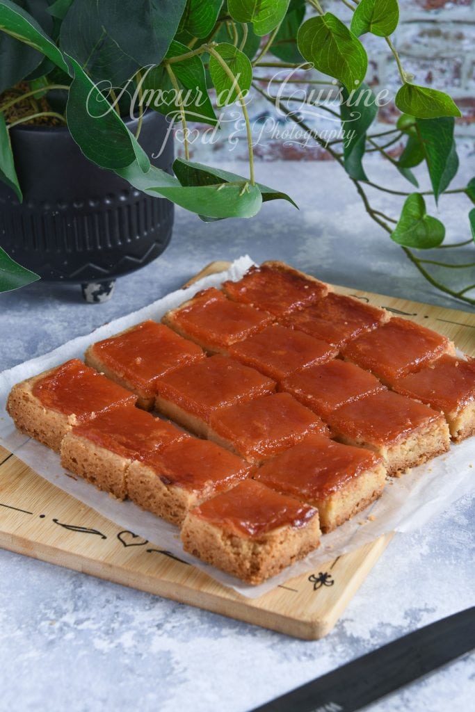 Carrés sablés à la pâte de coing, coupés et disposés sur une planche en bois, prêts à être dégustés, avec une plante verte en arrière-plan.