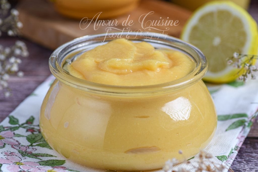 Close-up of honey quince sauce in a small glass jar, with a lemon half and decorative elements in the background.