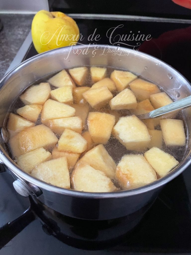 Morceaux de coing en cuisson dans une casserole remplie d’eau, avec une cuillère posée à l’intérieur.