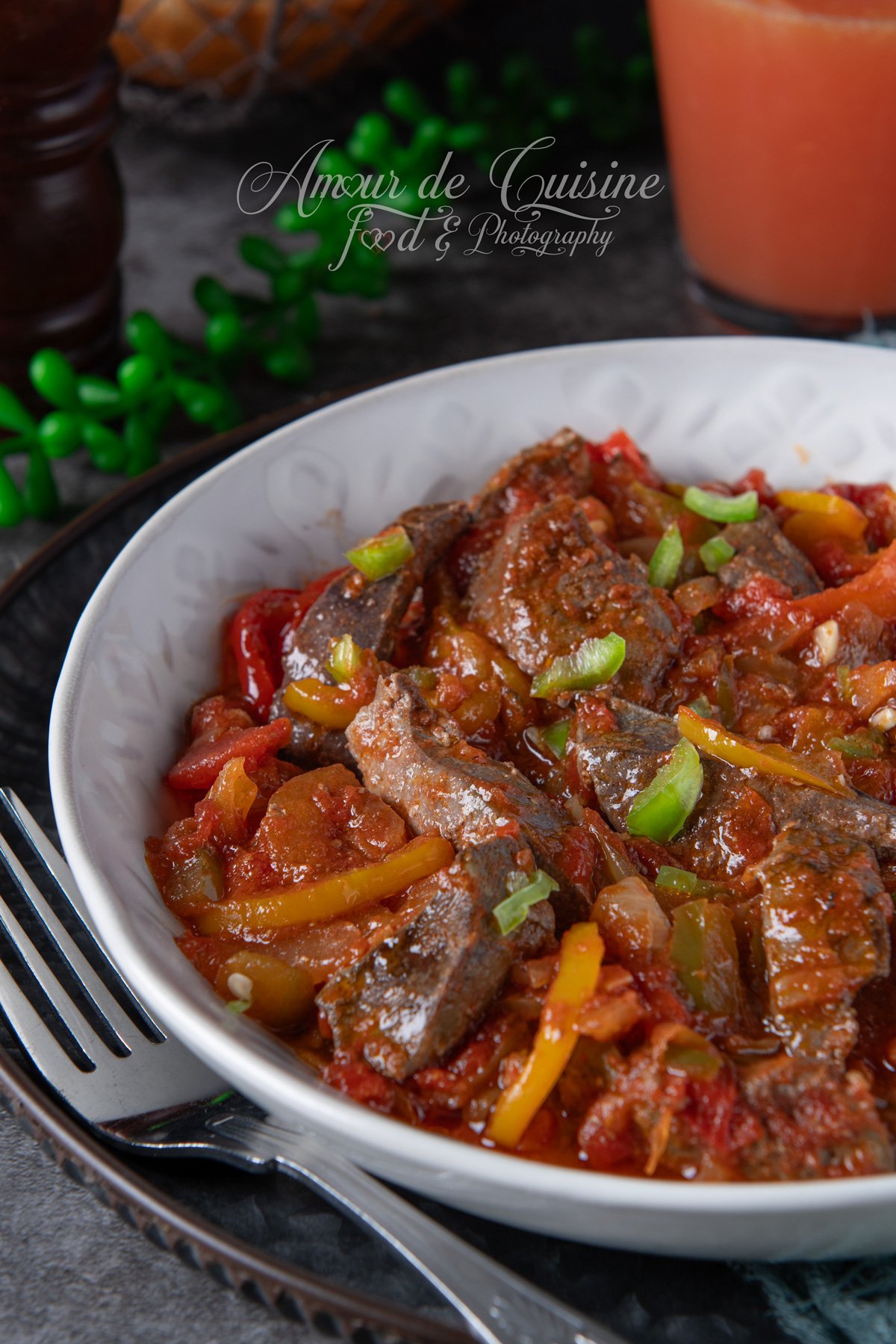 Gros plan sur une kebda à la chakchouka : foie d’agneau sauté dans une sauce tomate aux poivrons, garni de lamelles d’oignon vert, dans une assiette blanche.