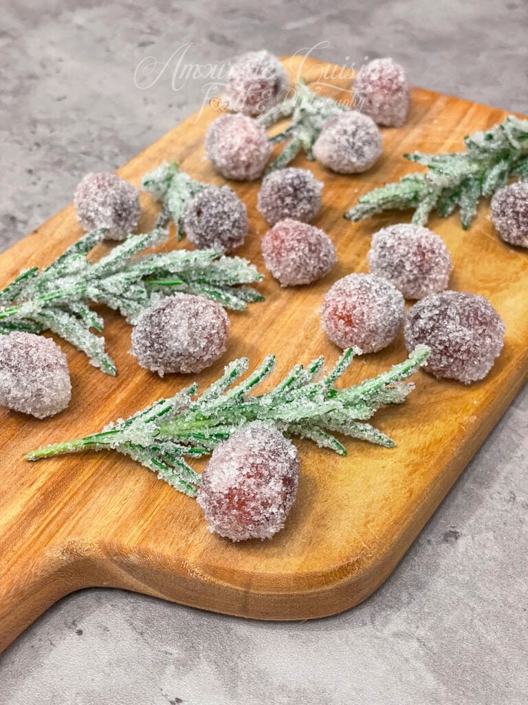 Canneberges et brins de romarin cristallisés au sucre, disposés sur une planche en bois, prêts à servir de décoration givrée pour une bûche de Noël ou un dessert de fête.