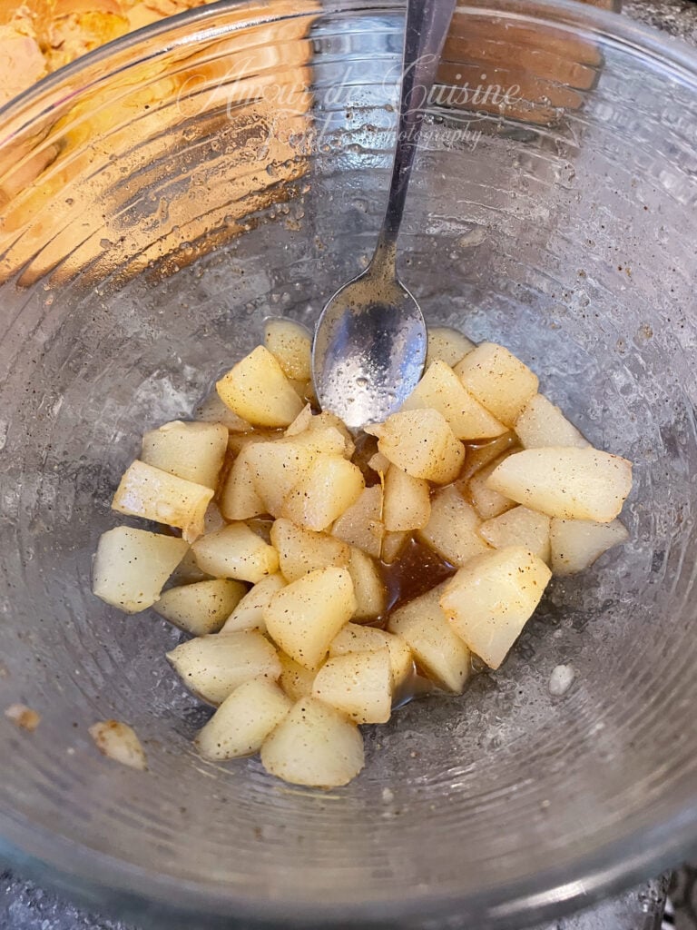 Dés de poires en conserve marinés à la cannelle et au gingembre dans un grand bol en verre, avec une cuillère, prêts à être utilisés pour garnir des verrines festives.