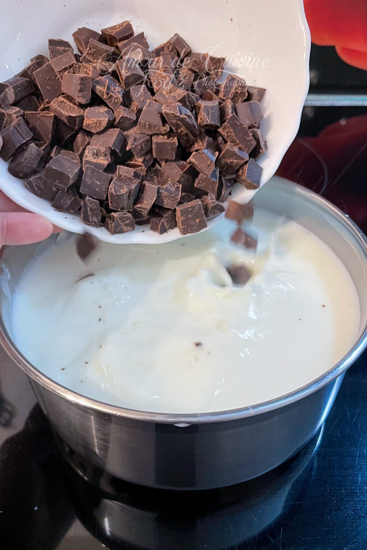 Des morceaux de chocolat noir sont versés dans une casserole de lait chaud sur une plaque de cuisson, première étape pour un chocolat chaud parisien épais.