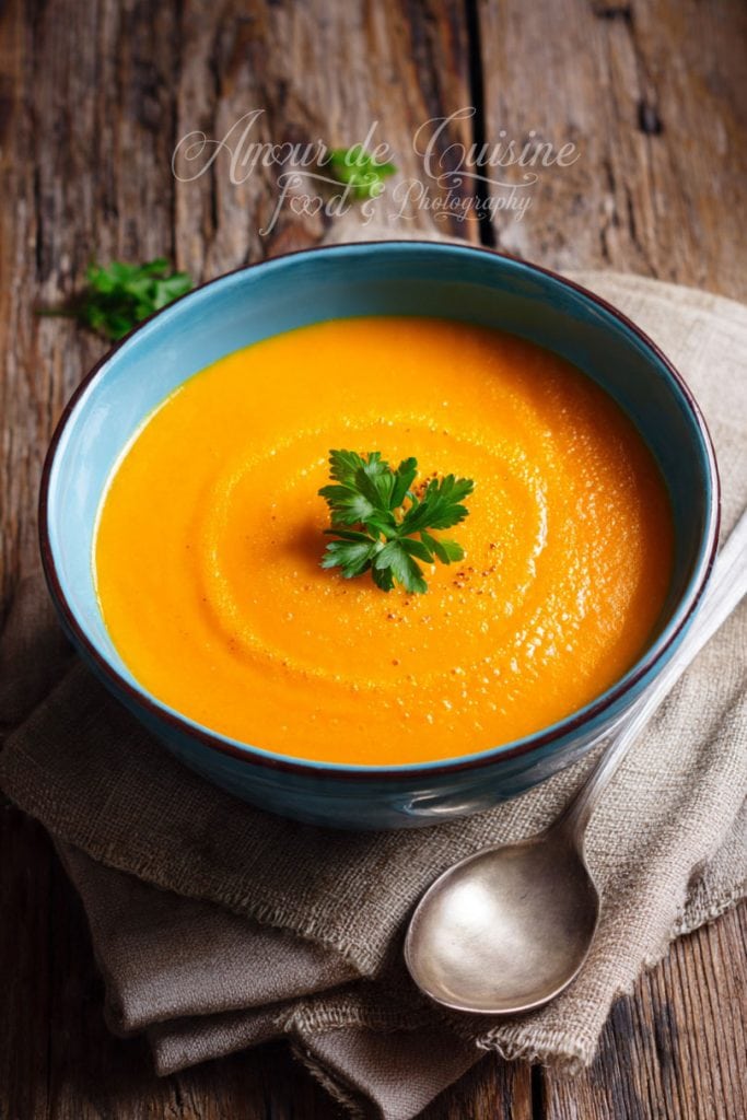 Bol de soupe de légumes rôtis, onctueuse et orangée, servie avec une touche de persil frais, posé sur un linge en lin sur une table rustique en bois.
