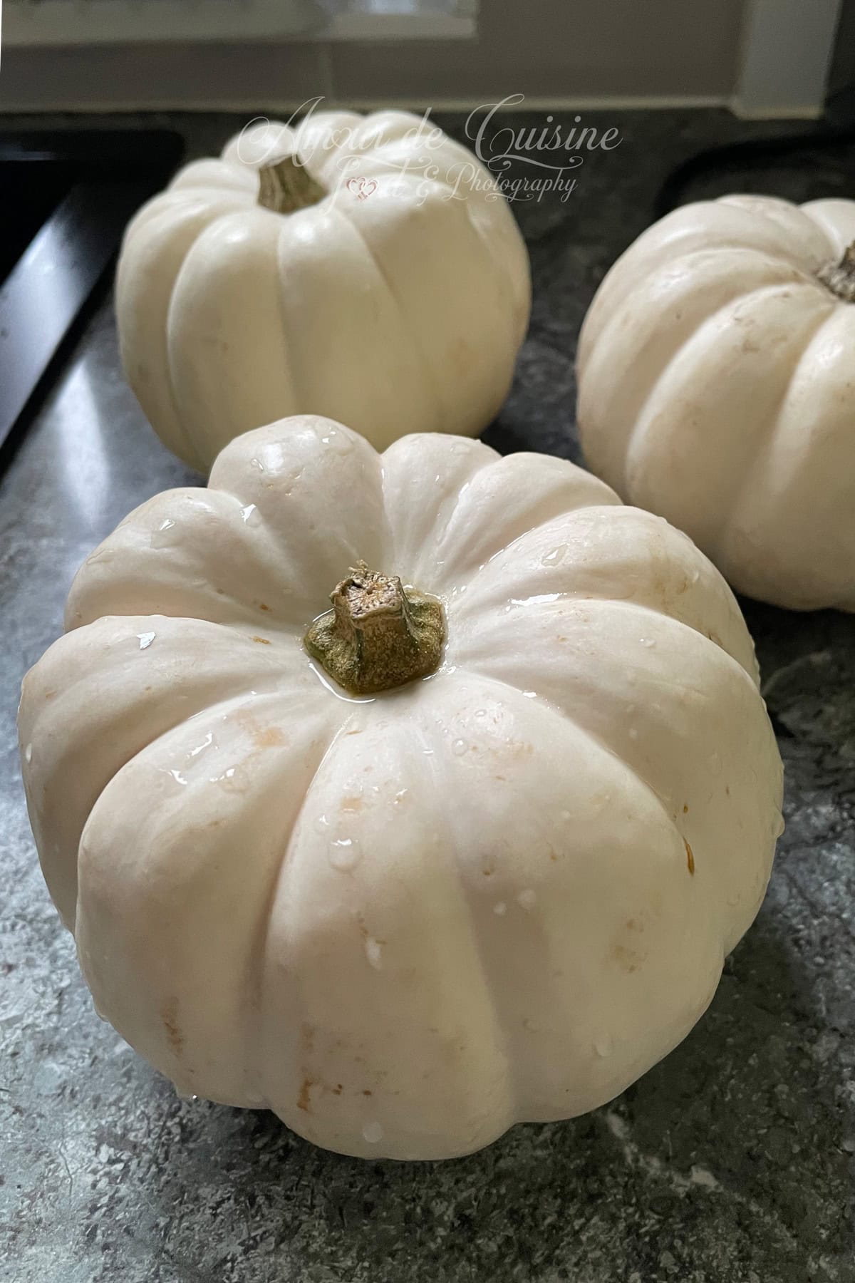 Trois petites courges blanches Casperita fraîchement lavées, avec des gouttes d’eau sur la peau, posées sur un plan de travail en cuisine.