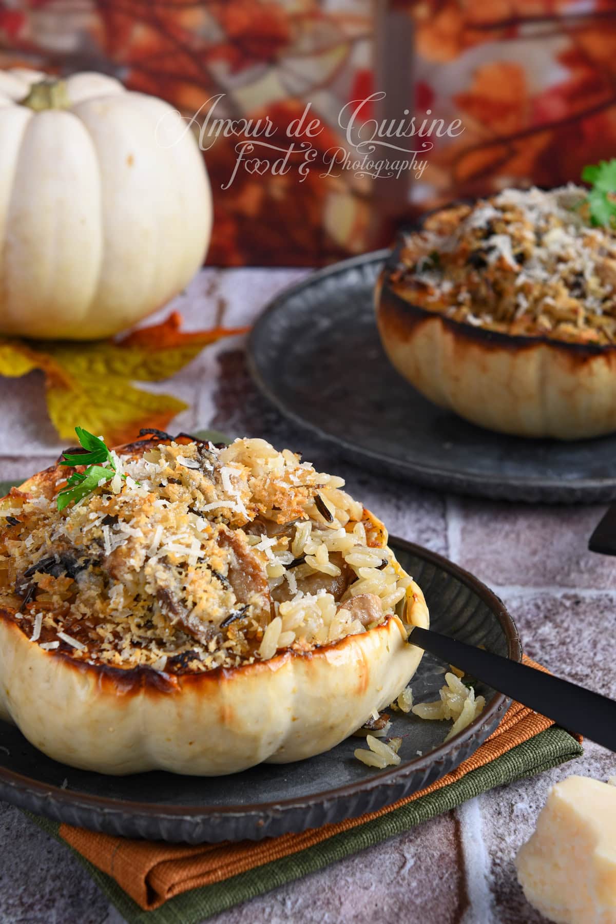 Courge blanche Casperita farcie au riz et champignons, gratinée au parmesan, avec une cuillère plantée dans la farce, posée sur une assiette sombre, décor automnal et seconde courge farcie en arrière-plan.
