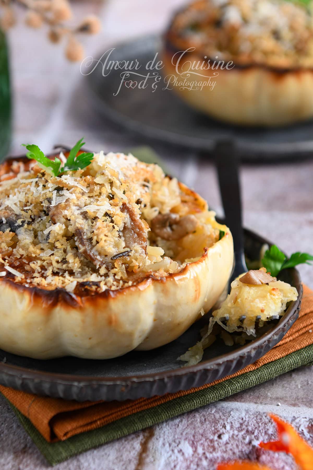 Courge blanche Casperita farcie au riz et champignons, gratinée au parmesan, photographiée de près sur une assiette, avec une cuillère et une bouchée de courge au premier plan, seconde courge floutée derrière.