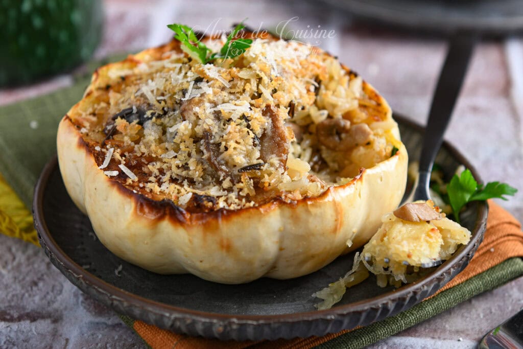 Gros plan sur une courge blanche Casperita farcie au riz et champignons, gratinée au parmesan, servie dans une assiette avec une bouchée prélevée à la cuillère et un brin de persil.
