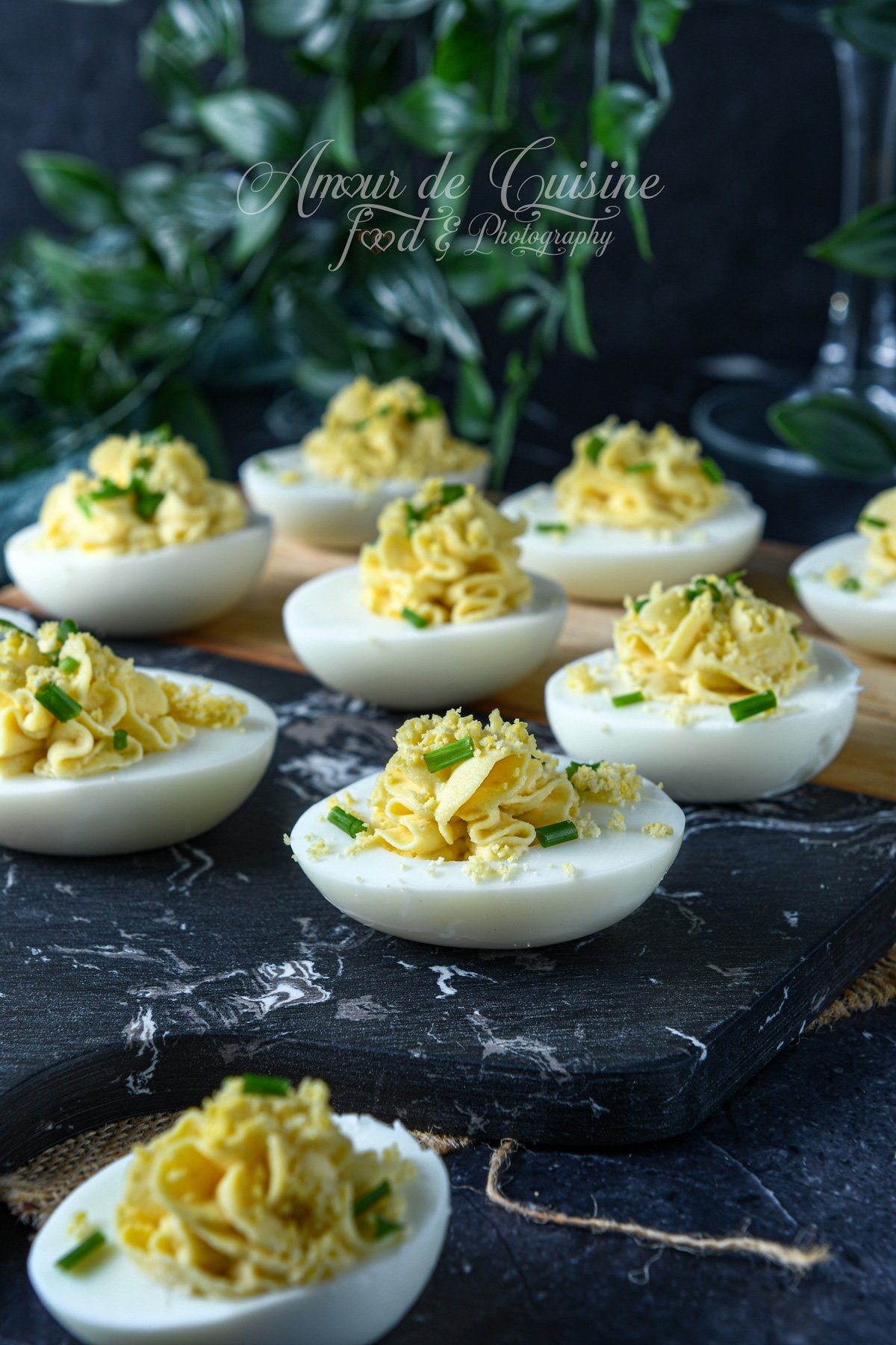 oeufs mimosa (œufs durs farcis à la mayonnaise) garnis en rosace, saupoudrés de jaune émietté et de ciboulette, présentés sur une planche effet marbre noir.