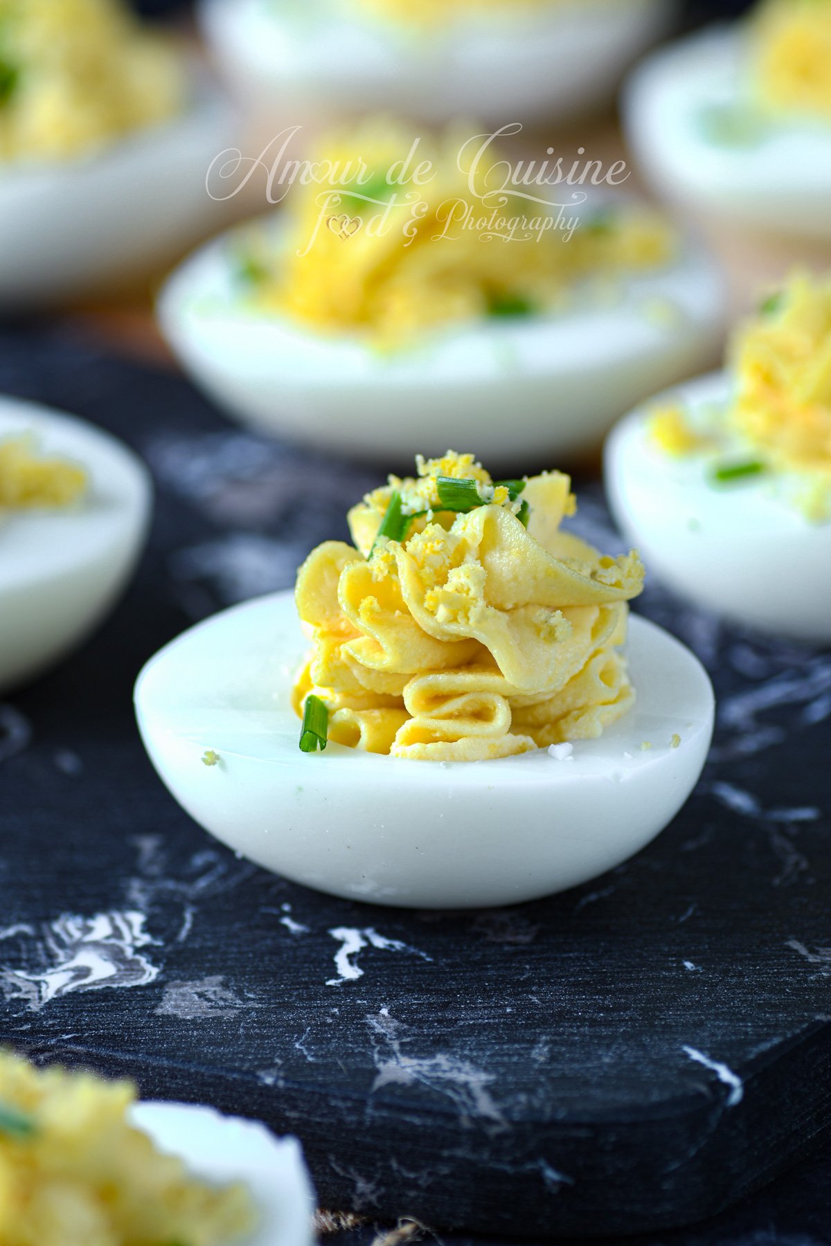 Gros plan sur un oeuf mimosa : demi-œuf dur garni d’une crème de jaune pochée en rosace, saupoudré de jaune émietté et de ciboulette, sur une planche effet marbre noir.