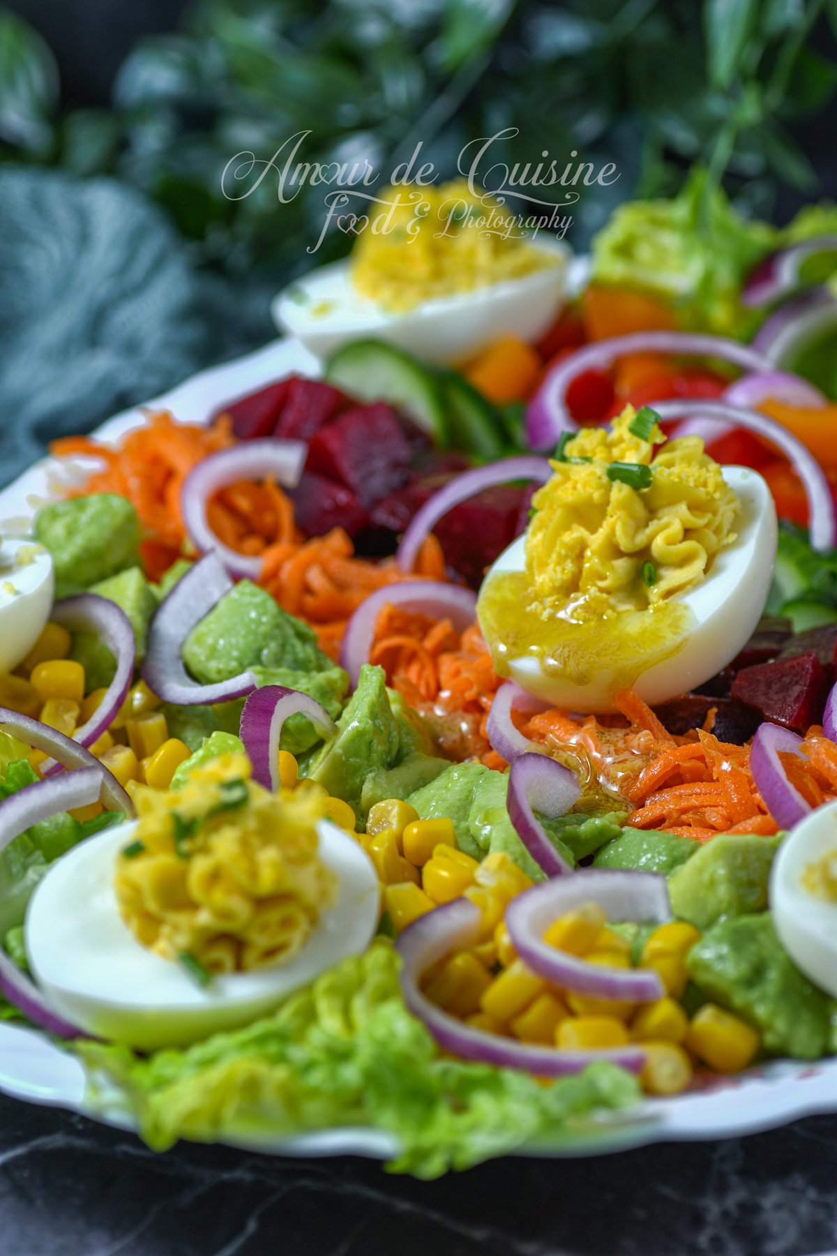 oeufs mimosa servis sur une salade de crudités colorée : laitue, maïs, avocat, carottes râpées, betterave, concombre et rondelles d’oignon rouge, avec une vinaigrette brillante.