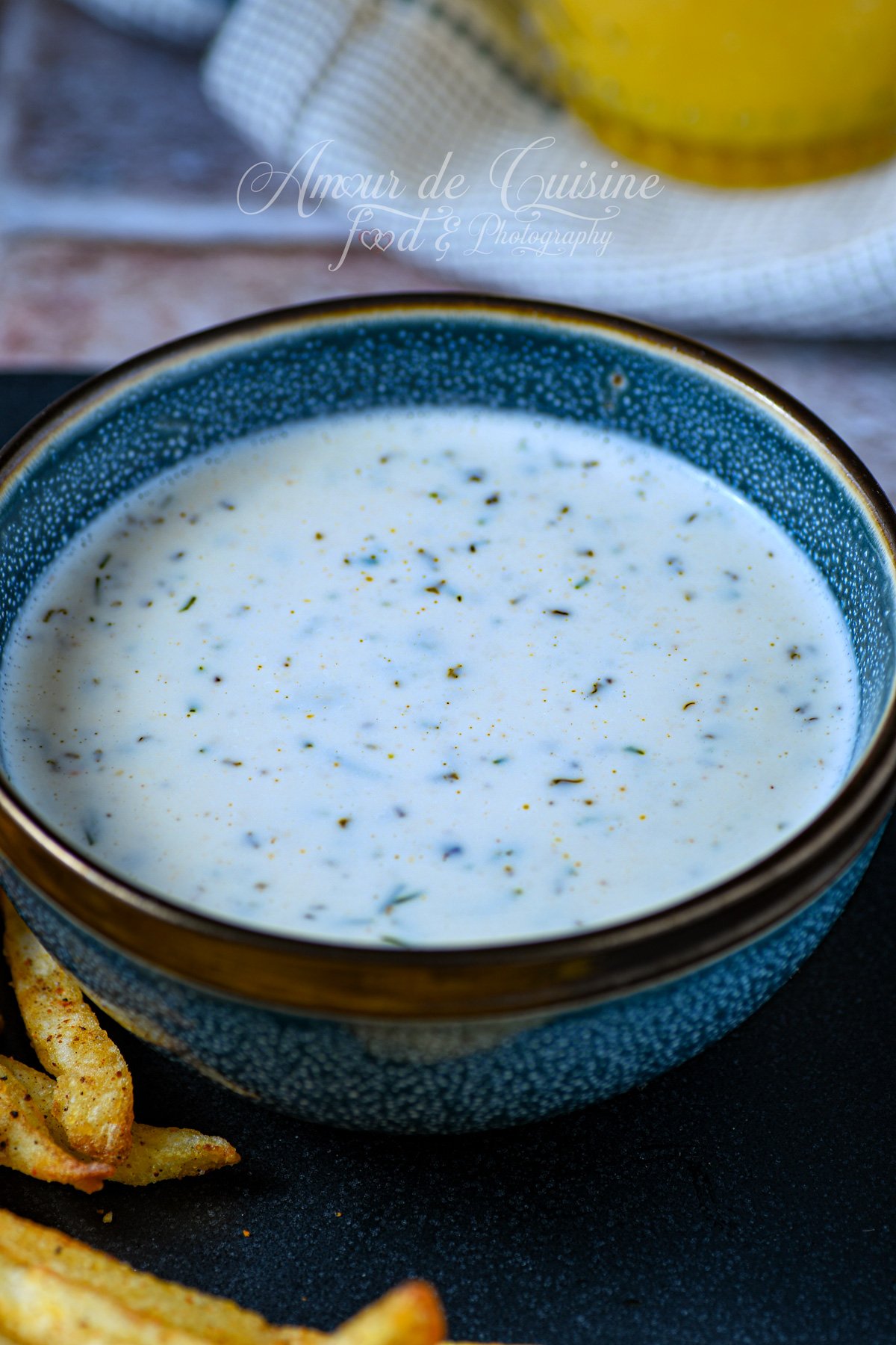 Bol de sauce ranch maison crémeuse, blanche et parsemée d’herbes, servie avec des frites croustillantes sur une assiette sombre.