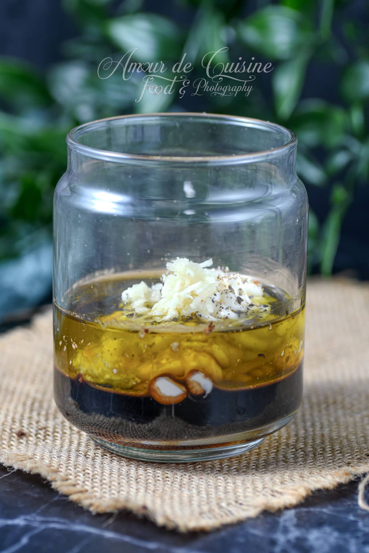 Bocal en verre avec huile d’olive et vinaigre balsamique, ail râpé, mayonnaise, sel et poivre, prêts à être secoués pour faire une vinaigrette sans moutarde.