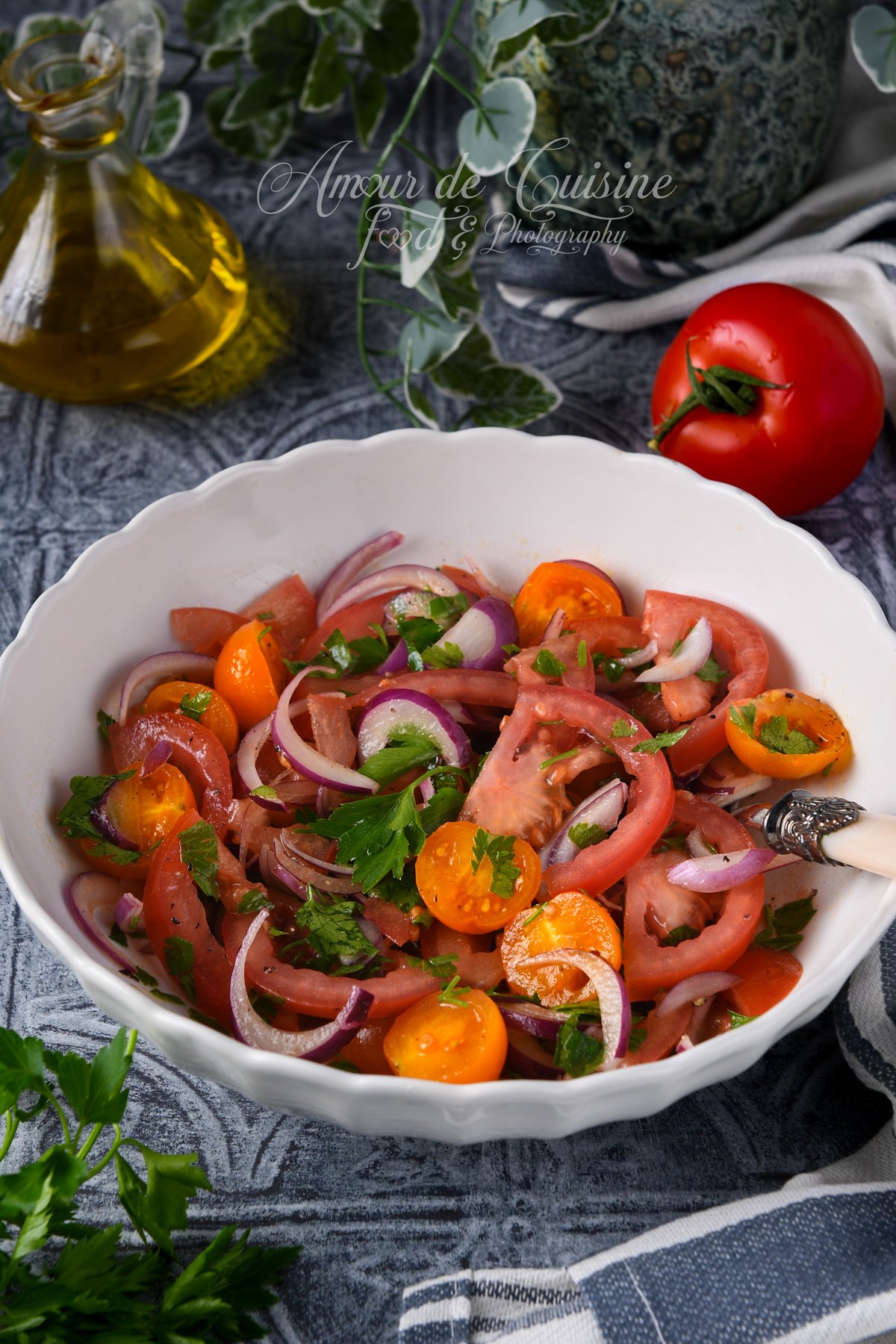 Salade de tomates fraîches (tomates rouges et tomates cerises orange) avec oignon rouge émincé et persil, servie dans un saladier blanc.