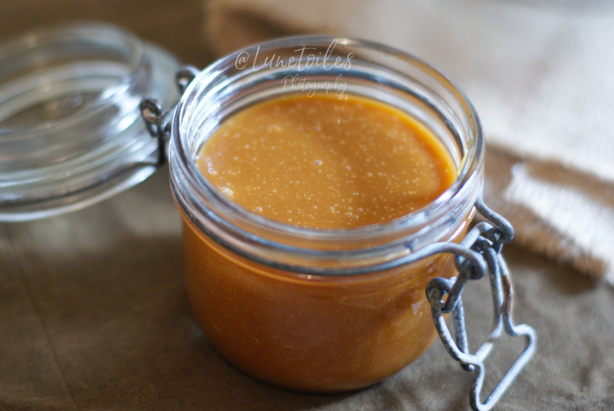 Glass jar filled with homemade salted butter caramel sauce, smooth and glossy texture, placed on a cloth.