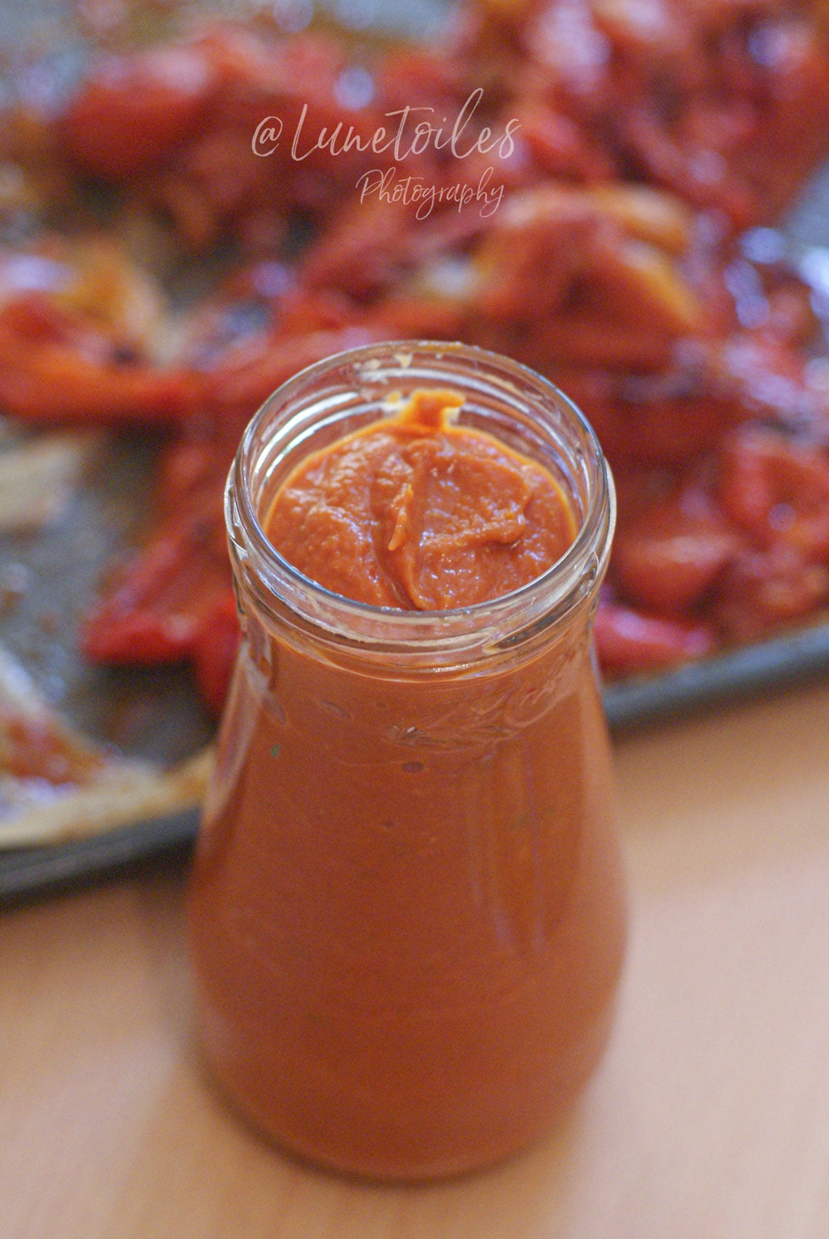 Pot de sauce aux tomates rôties maison, épaisse et onctueuse, avec les légumes rôtis au four en arrière-plan.