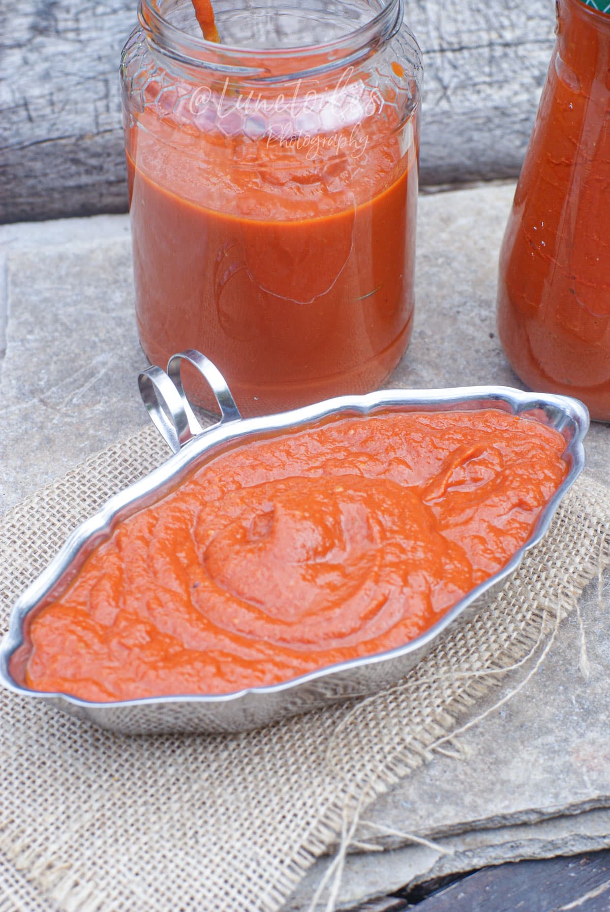 Sauce aux tomates rôties maison servie dans une saucière, avec des pots de sauce tomate en arrière-plan.