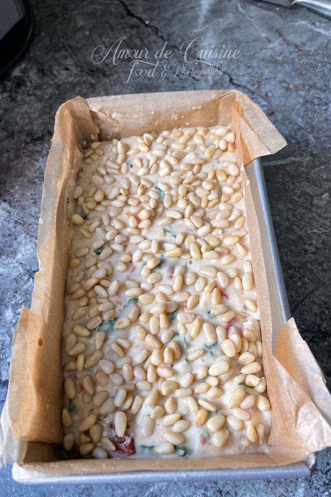 Pâte à cake salé aux tomates séchées, feta, basilic et pignons de pin versée dans un moule à cake avant cuisson.